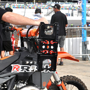 MX Racer pushing his dirt bike through the pits at Daytona with a pair of Adjustable Starting Blocks hanging on his handlebars.