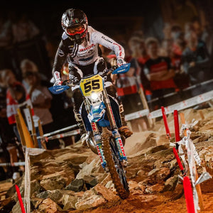 Enduro Racer moving through a rocky boulder section of the track coming straight at camera. He's wearing Risk Racing riding gear and his bike is equipped with Plews Tyres