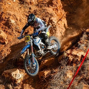 Enduro racer coming down a very rough hillside full of large rocks. He's wearing Risk Racing Gear and his bike is running Plews Tyres