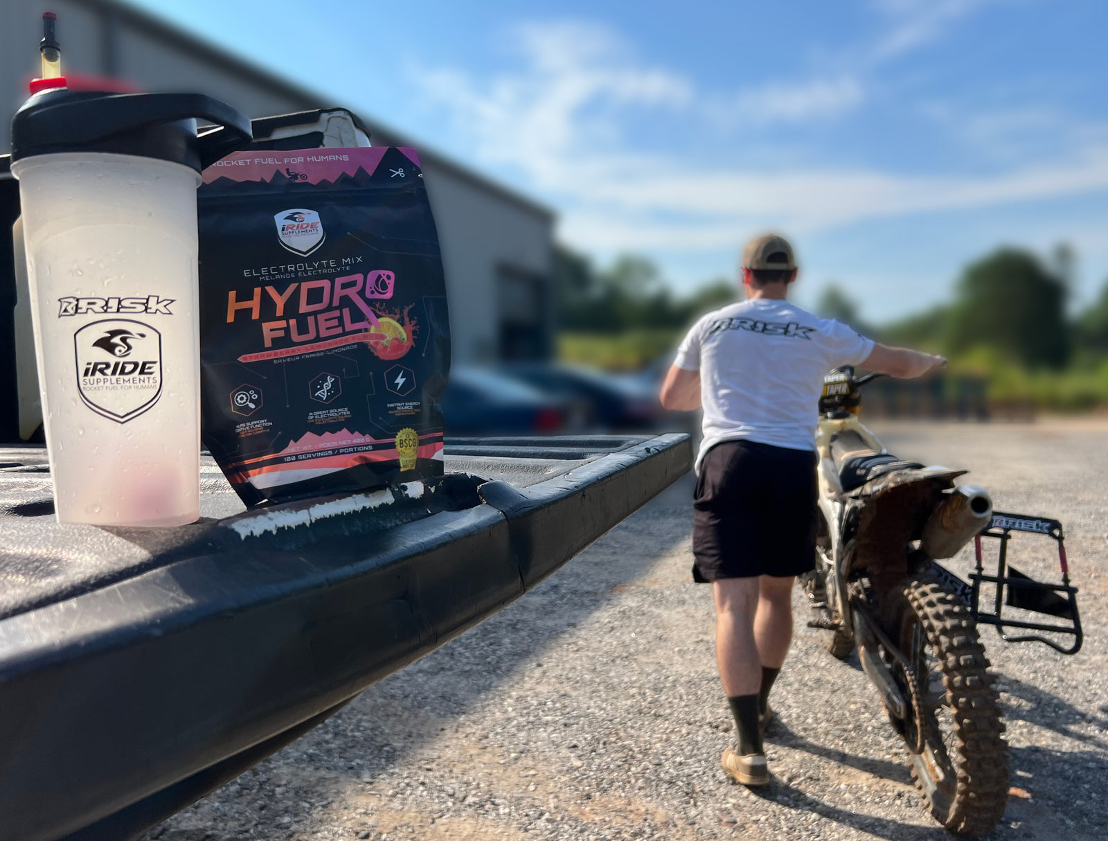MX rider walking pushing his bike away from the truck where a bag of Hydro Fuel powered supplements and a Risk Racing shaker bottle still sit