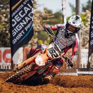 Motocross racer leaning their bike and body at a 45 degree angle while making a turn on a track.