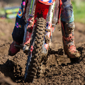 Motocross racer navigating through a rutted muddy area of a track. Pic is zoomed in on just the front tire and front forks of the motocross bike to highlight the Plews Tyres front tire.