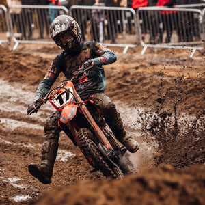 Very muddy motocross racer navigating a turn with very wet mud splashing away from them.