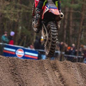 Close up of a motocross rider just leaving a muddy mx jump. back tire tread is very visible on the MX1 Hawkstone GP by Plews Tyres.